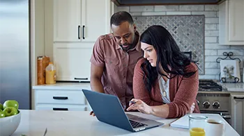 Standing in their kitchen, a couple check on their claim via their laptop.