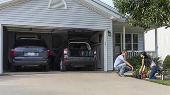 A couple plants flowers just outside their two-car garage. Combining their purchase of home and auto policies could save them money.